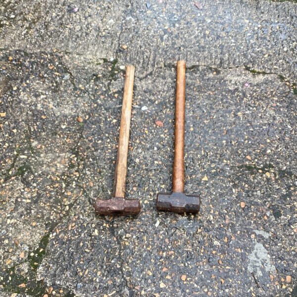 Pair of vintage sledgehammers with wooden handles and rusted metal heads.