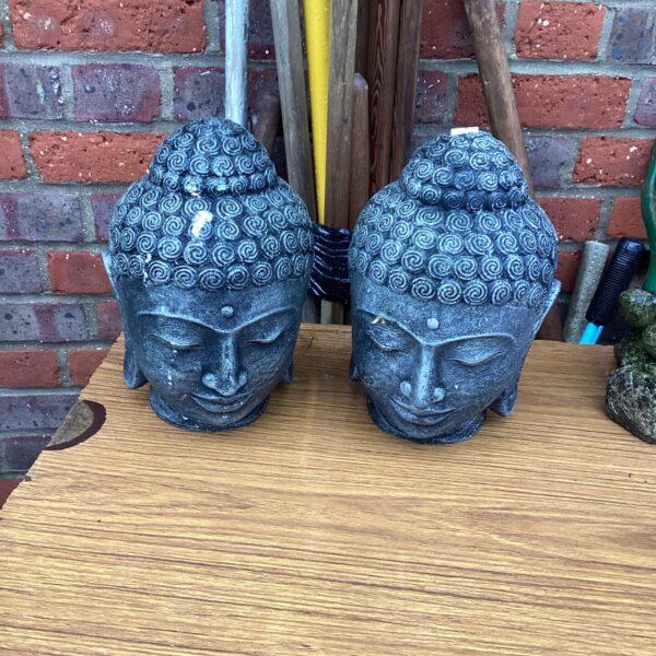 Two stone effect garden Buddha head ornaments in a garden setting.