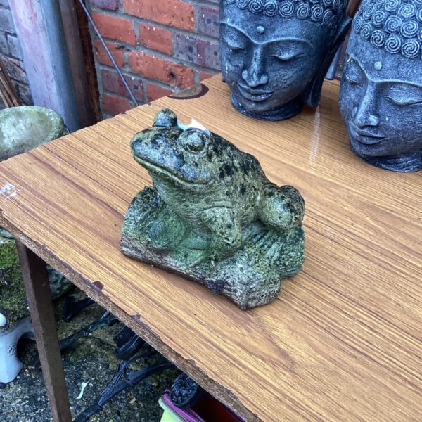 Close-up of a weathered stone garden frog statue.