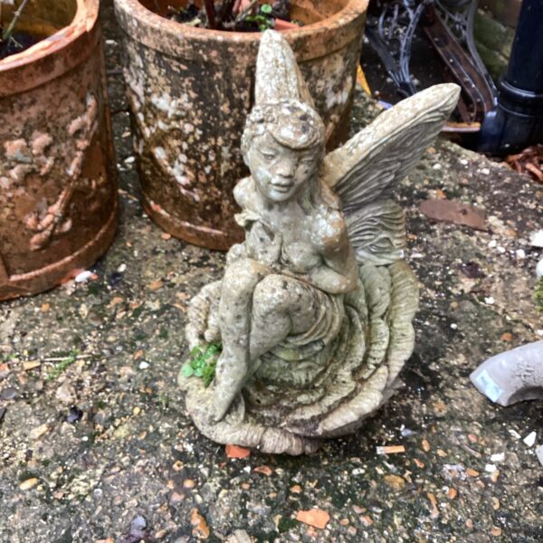 Vintage concrete garden fairy ornament in a garden setting.