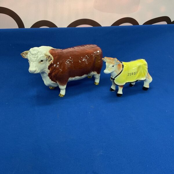 Vintage Beswick bull and cow porcelain figurines on blue background.