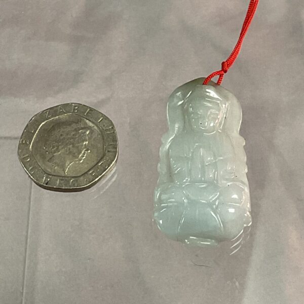 Pale green jade pendant with carved figure on red cord.