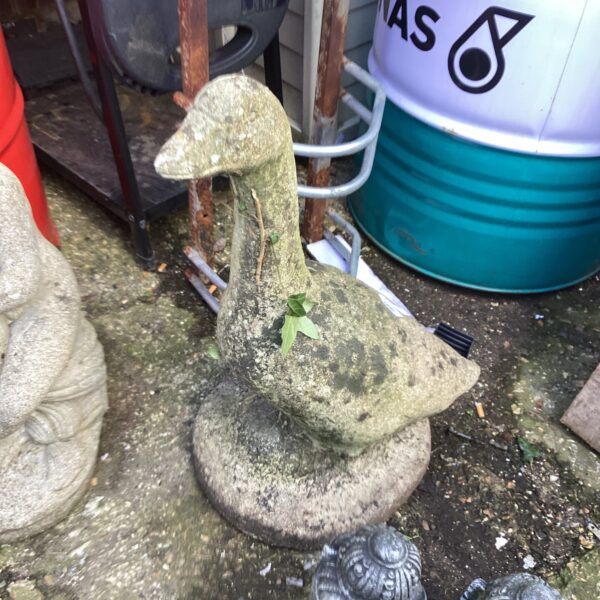 Stone goose garden ornament with weathered finish in outdoor setting.