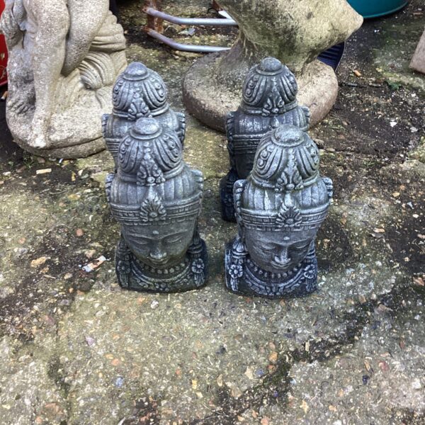 Set of four weathered stone Buddha head garden ornaments in a garden.