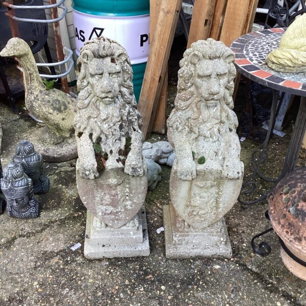Weathered stone garden lion ornaments in an outdoor setting.
