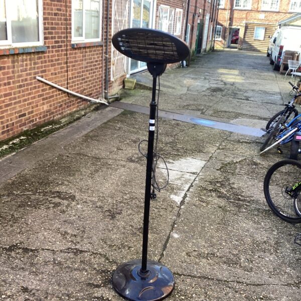 Black freestanding halogen patio heater in a garden setting.