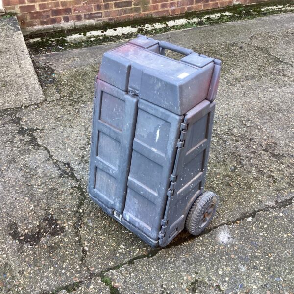 Grey portable tool box on wheels in a workshop setting.