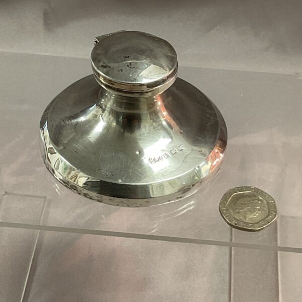 Antique sterling silver capstan inkwell on a tiled surface.