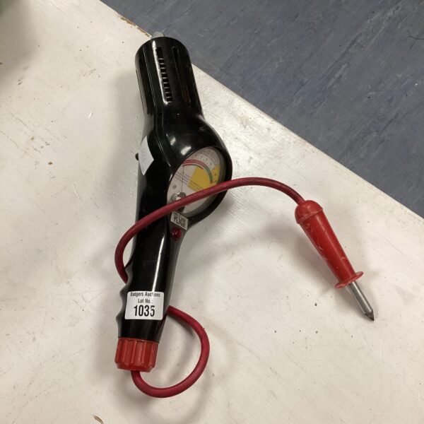Vintage car battery tester with red handle and gauge.