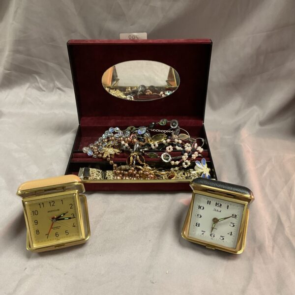 Vintage jewellery box with costume jewellery and travel clocks displayed.