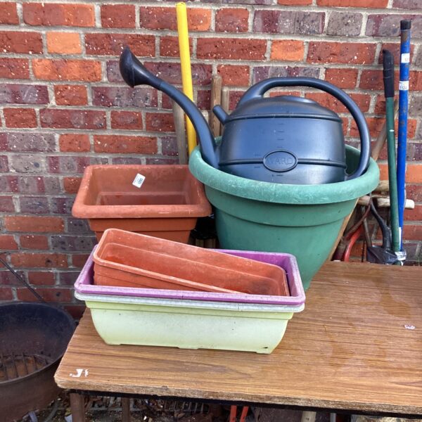 Plastic garden planters and a green watering can for outdoor use.