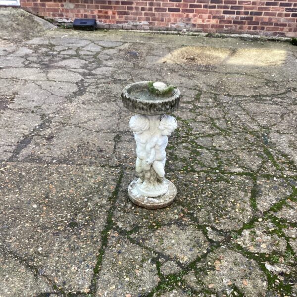 Vintage cherub bird bath in a garden setting.
