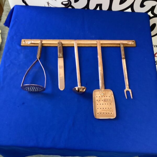 Vintage stainless steel hanging kitchen utensils set displayed on a blue background.