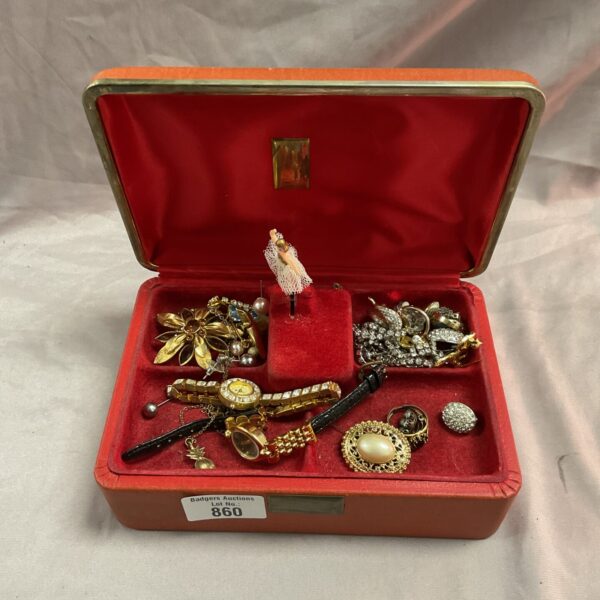 Vintage musical jewellery box open with assorted brooches inside.