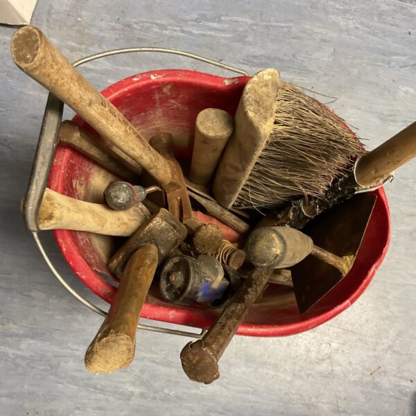 Red bucket filled with a lot of vintage builders tools.