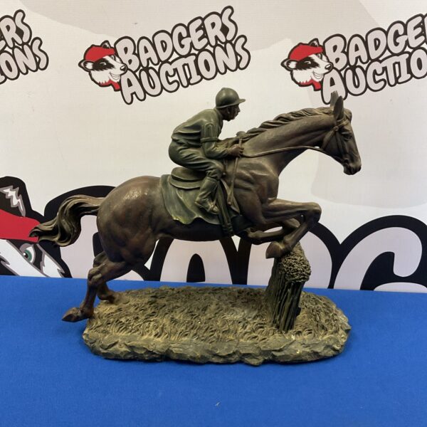 Detailed resin race horse sculpture jumping over a fence.