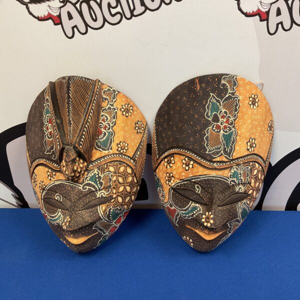 Pair of intricately carved Indonesian wooden masks with batik designs.