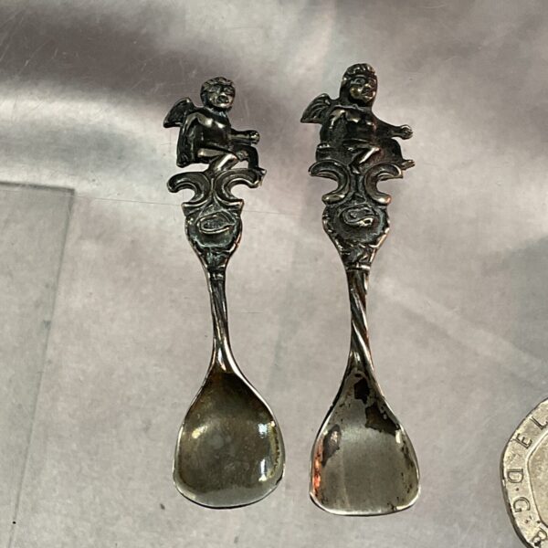 Antique sterling silver salt spoons with cherub decorations.