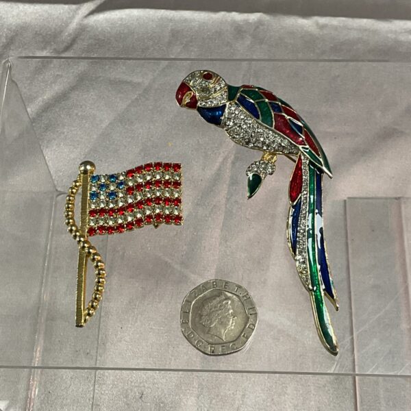 Vintage brooch pair featuring a jewelled flag and enamelled parrot.