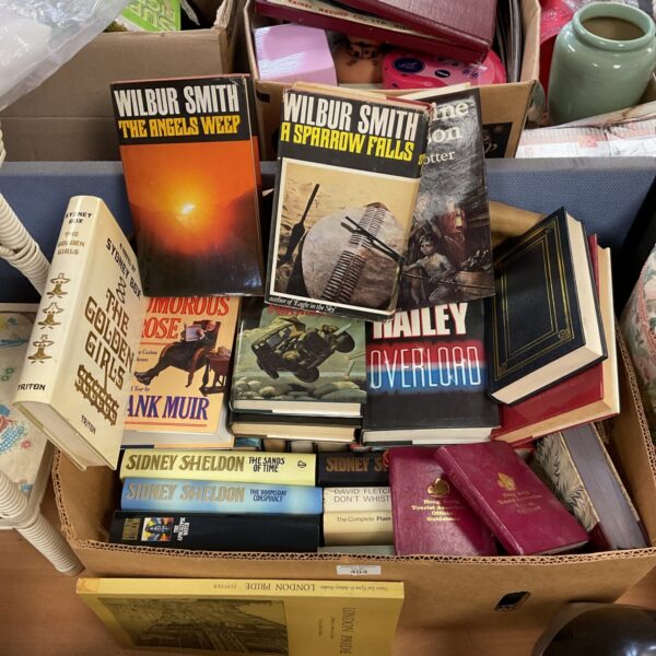 A stack of vintage Sidney Sheldon and Wilbur Smith paperback books.