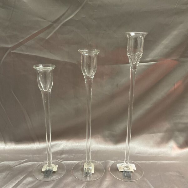 Set of three clear glass Broste Copenhagen candlesticks on a grey background.