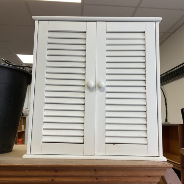 Small white farmhouse bathroom cabinet with slatted doors.