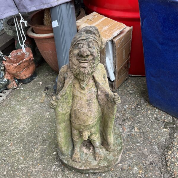 Cheeky flashing garden gnome statue in a garden setting.