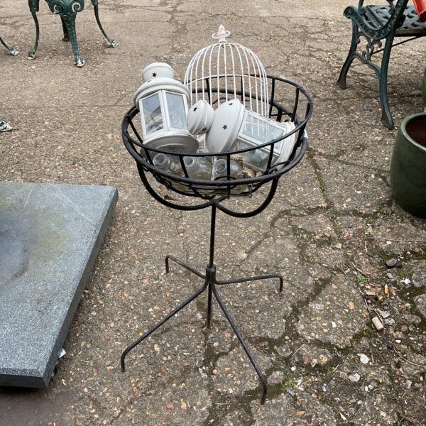 Wrought iron garden planter basket displaying candle lanterns outdoors.