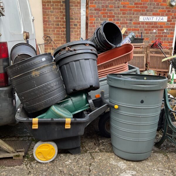 Large lot of plastic garden pots, compost bin, and wheelbarrow for gardening.