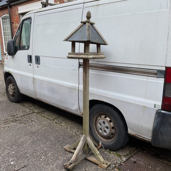 Vintage wooden bird table with slate roof in a garden setting.