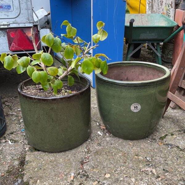 Two large green glazed planters in a garden setting.