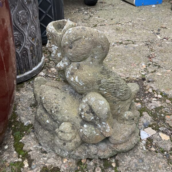 Weathered concrete garden duck ornament in a garden setting.