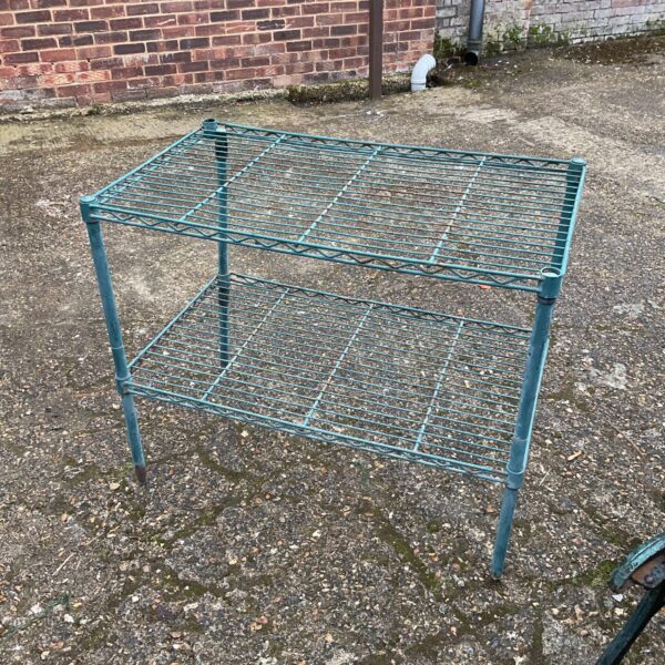 Vintage metal potting table with three tiers in a garden setting.