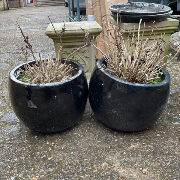 Two black plant pots in a garden setting.