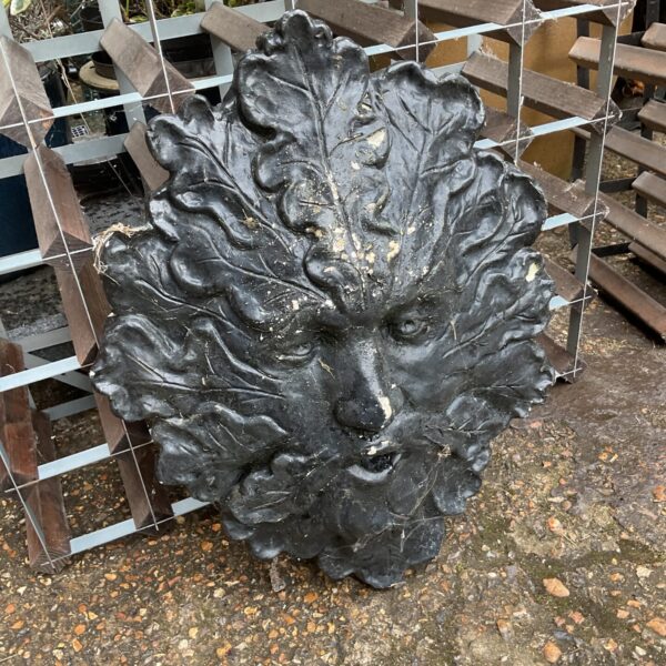 Weathered concrete green man face garden ornament with detailed foliage.