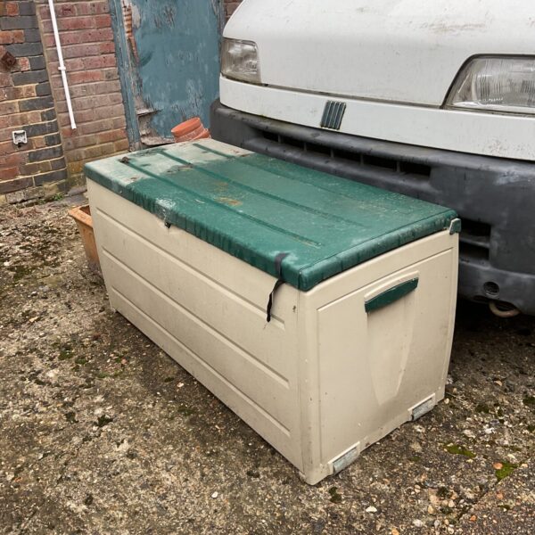 Weathered plastic garden storage bench in an outdoor setting.