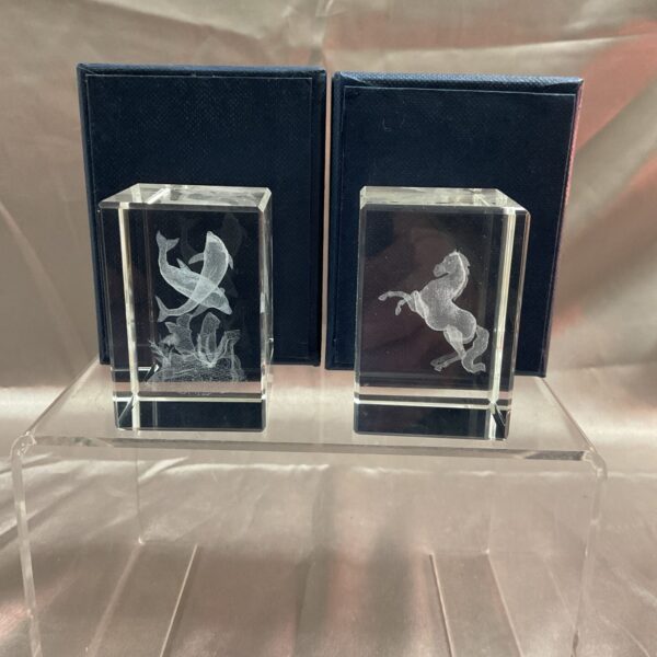 Clear glass paperweights featuring dolphins and a rearing horse.