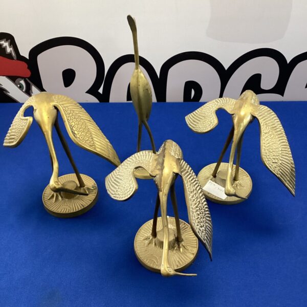 Four vintage brass crane birds on a blue background.