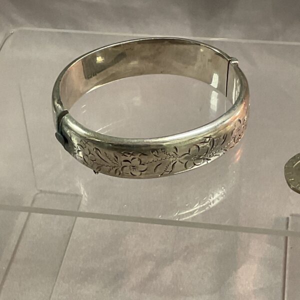 Delicate silver hinged bracelet with floral design.