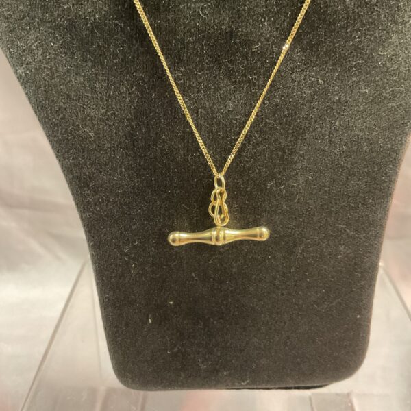 Delicate 9ct gold T bar necklace on a dark background.