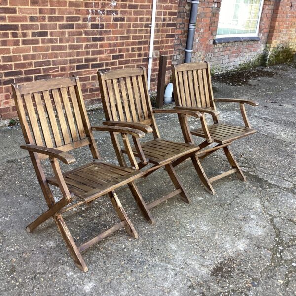 Three vintage teak garden chairs in a garden setting.