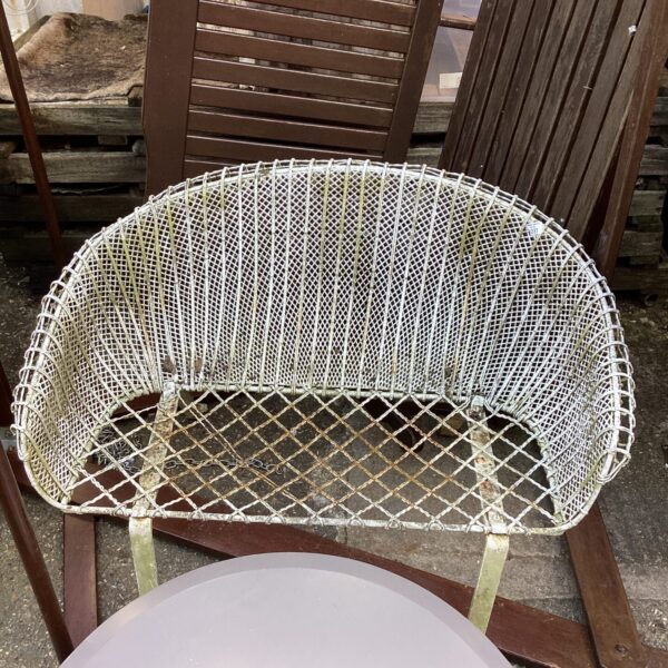 Vintage metal garden seat with woven detail in a garden setting.