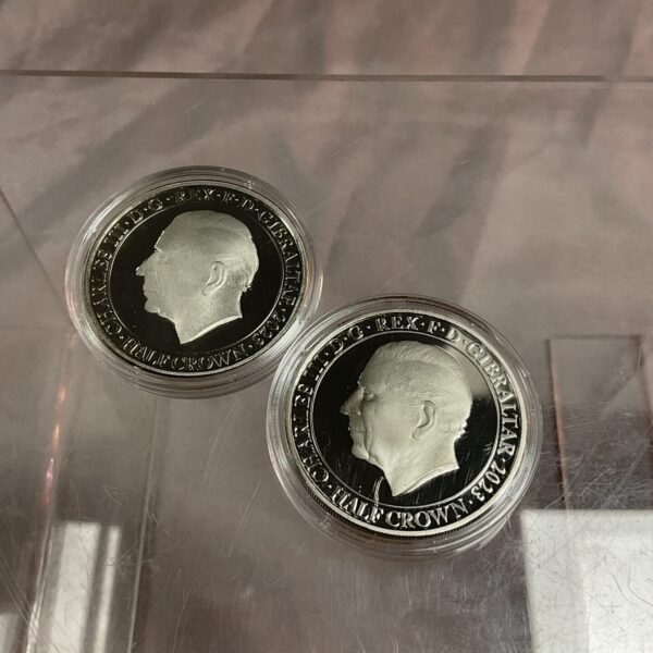 Two Charles 2023 Half Crown coins on reflective surface.
