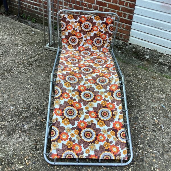 Vibrant vintage sun lounger with floral pattern in garden setting.