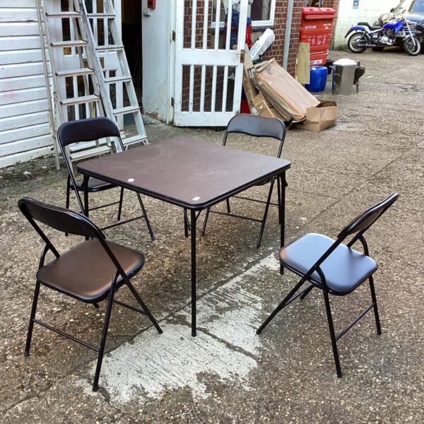 Black folding table and four chairs in a garden setting.