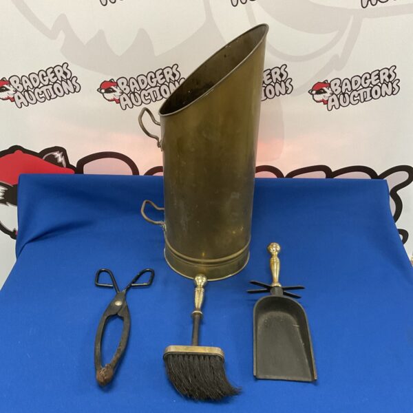 Vintage brass coal scuttle with fireplace tools displayed on a dark surface.