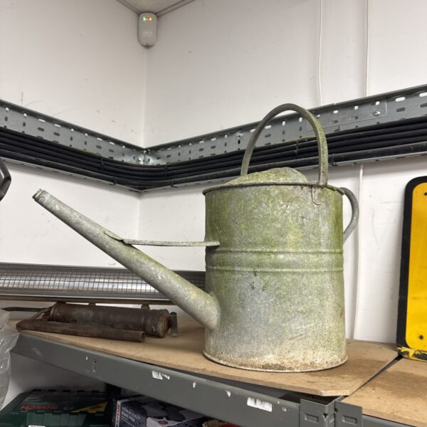 Vintage galvanised watering can on a metal shelf.