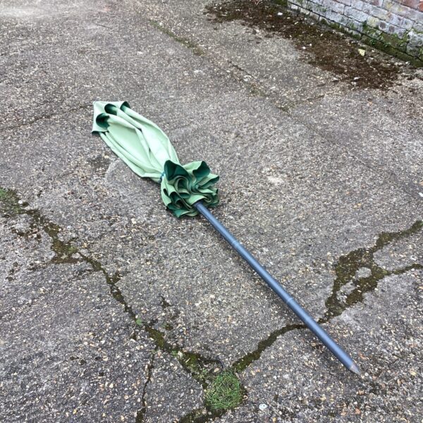 Green garden parasol standing on a paved surface.