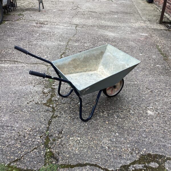 Galvanised steel wheelbarrow in a garden setting, ready for use.