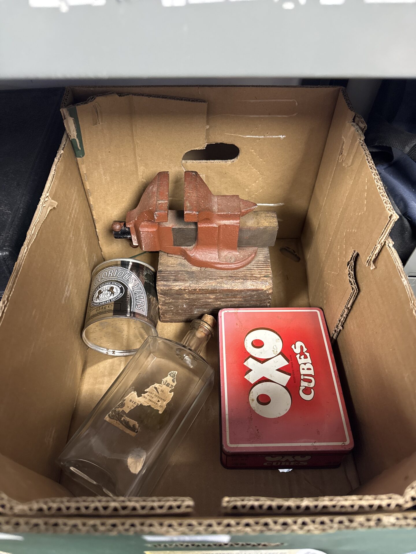 911 Two empty tins, a glass bottle & small bench vice
